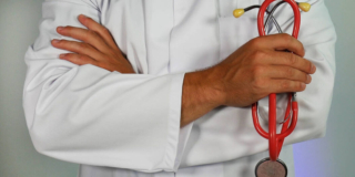 Doctor in a white coat with their arms crossed holding a red stethoscope