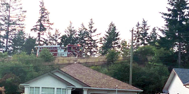 A fire truck is parked on a hill behind a house.