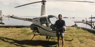 Teddy Masales stands in front of his small helicopter, which is parked on a grass patch.