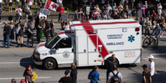 People with signs stand in the street in front of an ambulance with a patient in it.