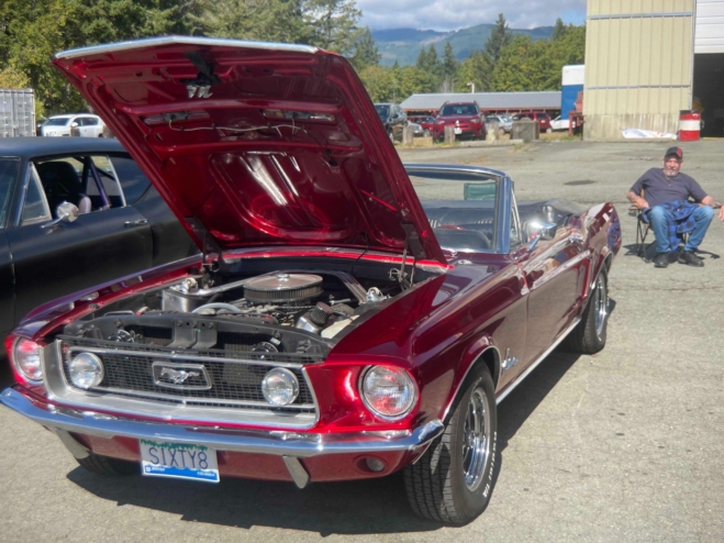 A red classic Mustang parked with its hood propped up.