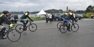 Cyclists ride off while people wave on a cloudy day.