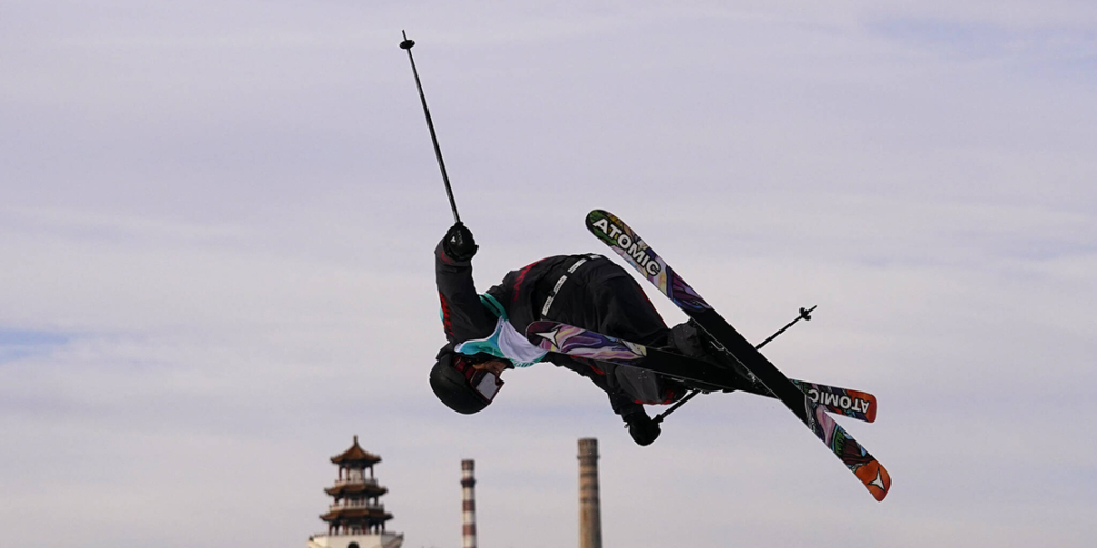Teal Harle twisting in mid-air with his skiis. Traditional Chinese buildings are in the distance.