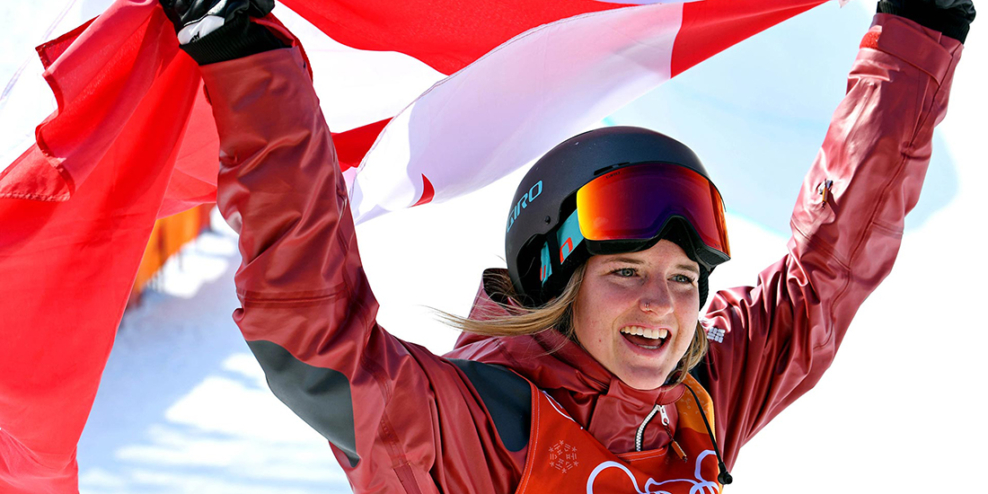 Cassie Sharpe smiles while holding a Canadian flag above her head.