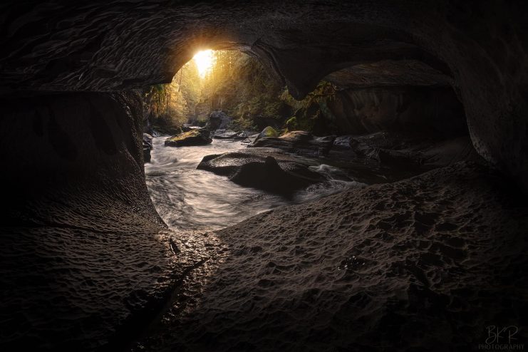 A photo from inside the Little Huson Caves. The light coming into the cave illuminates the walls and the stream that flows out of the cave.