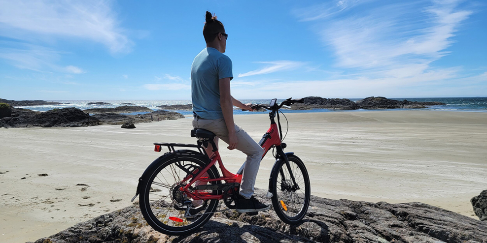A fit young man sits on an E-bike and looks out at a sandy beach and rocky outcroppings.