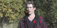 Kohen Gilken speaks for a news camera wearing a flannel and a Rememberance Day poppy.