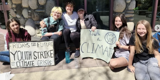 A group of students sit with signs calling for local climate action.
