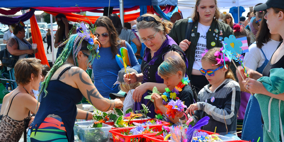 Folks in brightly coloured clothing do crafts and celebrate at the Pride event at Spirit Square.