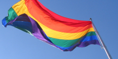 A rainbow flag flies on a sunny day.