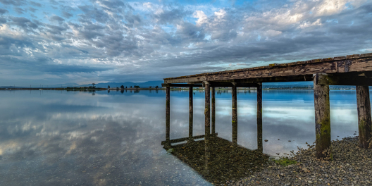 A wooden pier in Comox is reflected on the water.