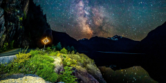 The Milky Way is reflected onto a lake with mountains silhouetted in the distance.
