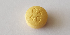 Closeup: a yellow OxyContin tablet sits alone on a white background.