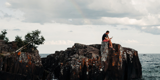 A man sits alone on a rock outcropping while looking at his phone.