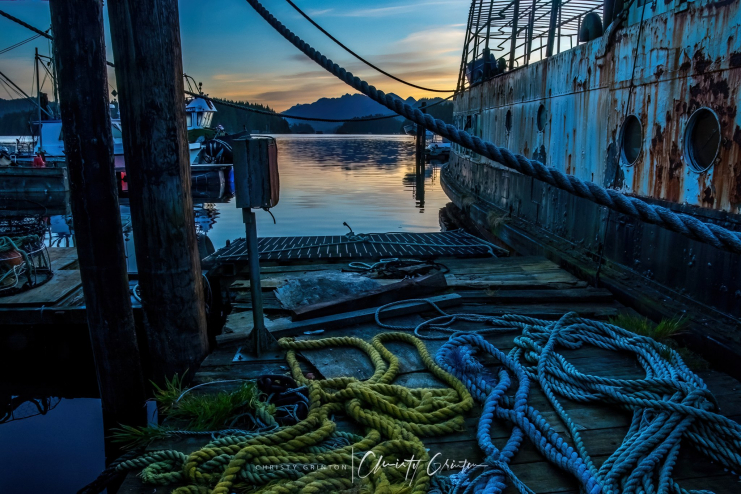 Early morning light hits coiled fishing ropes on a dock with hills in the background.