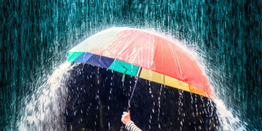 Rain pours down on a multi-coloured umbrella.