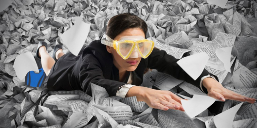 A woman wearing scuba goggles and flippers swims through a sea of paperwork.
