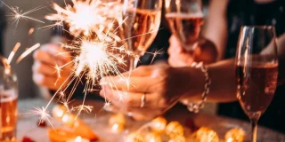 A closeup of hands wearing fancy bangles and holding sparklers alongside glasses of champagne.