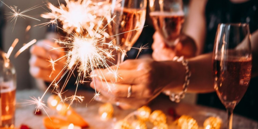 A closeup of hands wearing fancy bangles and holding sparklers alongside glasses of champagne.