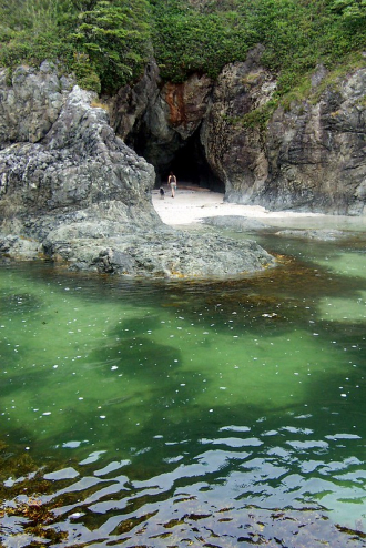 A drone shot of a woman and a dog walking into the Keeha Beach cave near Bamfield.