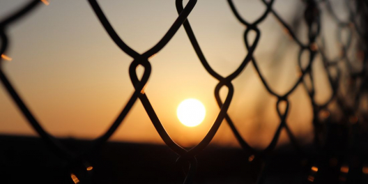 Sun sets behind a chain link fence.