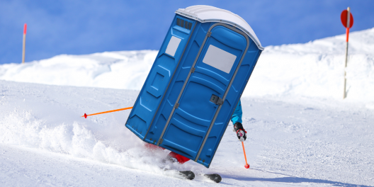 A big blue porta-potty skis down a hill.