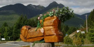A photo of the big wooden boot that was carved using a chainsaw. There are mountains in the background.
