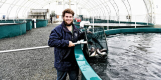 A man stands smiling in front of a pool in the land-based fish farm.