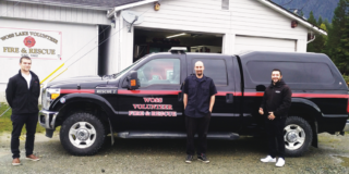 Three members stand outside the fire hall in front of their new rescue truck on a cloudy day.