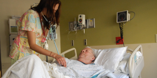 A nurse attends to an elderly person in a hospital bed.