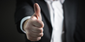 A closeup of a man's hand giving the thumbs up sign. He's wearing a business suit.