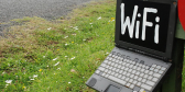 An old laptop is perched on a stoop outdoors. It has the word "WiFi" written on the screen in white paint.