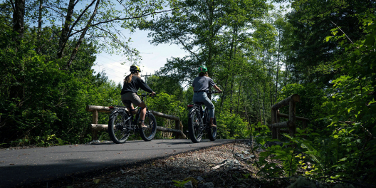 Two people on e-bikes cruise down the new ʔapsčiik t̓ašii multi-use trail in Pacific Rim National Park.