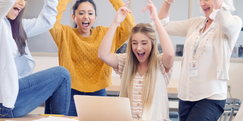 Three teens and a teacher cheer at something exciting on a laptop screen.