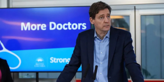 David Eby stands in front of a sign that reads "More Doctors."