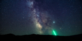 The Milky Way above the horizon with a bright green meteor streaking toward the earth.