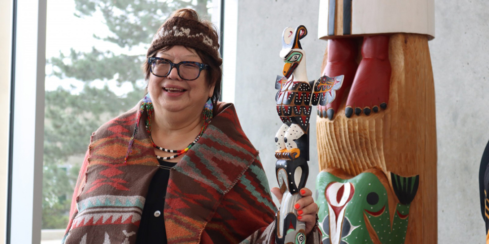 Judith Sayers beams while wearing a traditional cape and carrying her new talking stick.