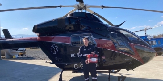 Critical care paramedic Brian Gill is pictured beside a BCEHS helicopter. (BC Emergency Health Services)
