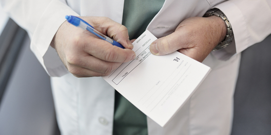 A closeup of a doctor's hands writing on a pad of prescription paper.