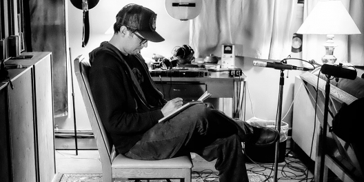A black-and-white photo of Corwin Fox writing on a notepad in a studio.