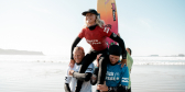 Two young surfers carry another surfer on top of their shoulders after she won her surfing competition.
