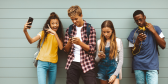 Four young teenagers take selfies and check out their phones against a school wall.