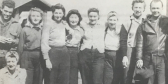 A black-and-white photo of the Plywood Girls standing in a line for the camera on a sunny day.