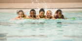 A bunch of kids smile in a swimming pool.