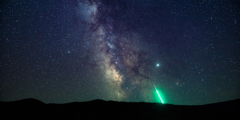 The Milky Way above the horizon with a bright green meteor streaking toward the earth.