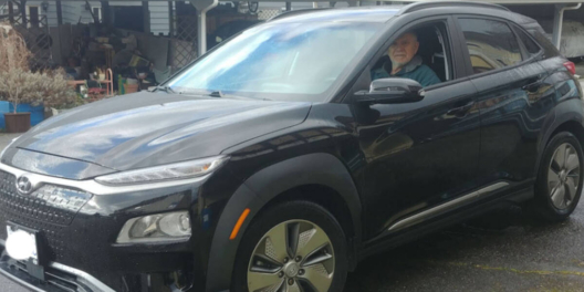 An older gentleman sits in the driver's seat of his Kona EV. He looks pretty pleased with himself.