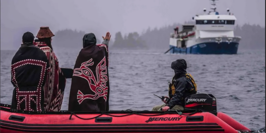 Members of the 'Namgis First Nation on a dingy raise their hand to stop an oncoming fishing boat.