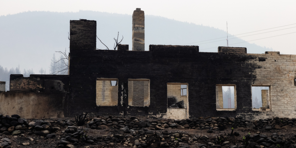 A burned out building sits in the hazy smoke of a forest fire.