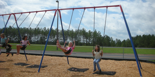 Girls play on a swingset on a sunny day.