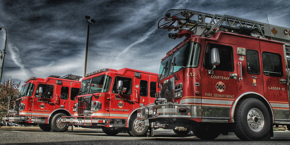 Three Courtenay fire trucks sit parked against a moody sky.